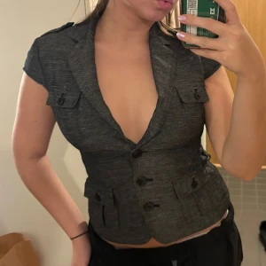 Figursydd väst  - Snygg grå väst med korta ärmar och v-ringning. Figursydd modell.