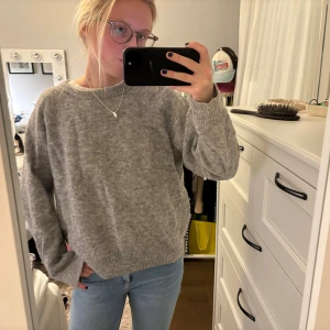 Grå stickad tröja Carin Wester M - Mysig grå stickad tröja från Carin Wester i storlek M. Tröjan har en rund halsringning, långärmade ärmar och en loose passform. Materialet är mjukt och fluffigt, perfekt för kyliga dagar. Enkel och stilren design som är lätt att matcha med jeans eller kjol.