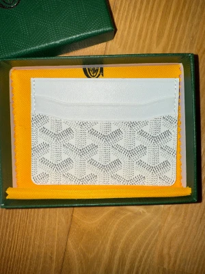 Korthållare  - En vit plånbok är den perfekta kombinationen av klassisk elegans och modern lyx. Den ikoniska handmålade chevron-designen i vitt skapar ett stilrent, exklusivt uttryck som lyfter varje outfit. Med noggrant hantverk, lätt men slitstark canvas och smart organiserade fack är det här accessoaren för dig som vill bära något både tidlöst och unikt. Ett statement av ren sofistikation – varje dag