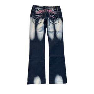 Blue Queen jeans med broderi och blekta detaljer - Mörkblå jeans från Blue Queen med kraftigt blekta partier och rosa broderi samt strass på bakfickorna. Snygg bootcut-modell med låg midja och raka ben. Jeansmaterialet är klassiskt och detaljerna ger en unik look. Perfekta för dig som vill sticka ut.