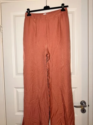 Rosa wide byxor från NA-KD Reborn - Snygga ljusrosa byxor från NA-KD Reborn i storlek 40. De har en bred passform med hög midja och är gjorda i ett glansigt, mjukt material som ger en skön känsla. Perfekta för dig som gillar avslappnad och trendig stil.