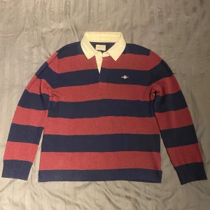Gant stickad rugger rugbytröja  - Stickad rugbytröja från gant i klassisk röd/blå färgkombination. Vit krage och gantskölden på bröstet samt slits i nedkant. Otroligt mjukt och skönt material. Skriv om det skulle va några frågor //Hugo
