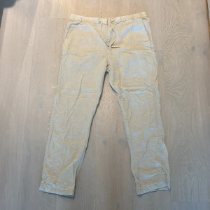 Beiga linnebyxor från H&M med snörning - Snygga beiga linnebyxor från H&M i regular fit. Byxorna har elastisk midja med snörning och sidfickor. Aldrig använda, nypris 450kr.