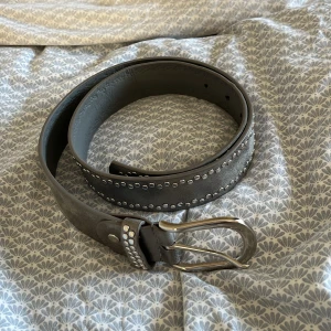 Skärp silver - Snyggt grått bälte med silverfärgade nitar längs kanterna och en cool silverspänne. Bältet är brett, vilket ger en schysst och robust känsla. Perfekt för att ge outfiten lite edge med metalliska detaljer. Passar s/xs och är i fint skick