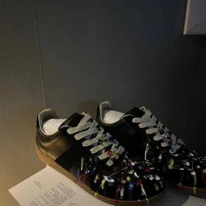 Gats - Svarta sneakers från Valentino Garavani med coola färgstänk i blått, rött, gult och vitt över hela ovandelen. Skorna har vita snören och en klassisk gummisula i beige. Perfekt för dig som vill sticka ut med en unik och kreativ stil.