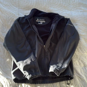 Svart jacka från Columbia, - Svart jacka från Columbia med stilren design och hög krage. Jackan har dragkedja framtill, två sidofickor med dragkedja och justerbar nederkant med snörning. Materialet är syntet och insidan är fodrad med mjuk fleece. Perfekt för dig som gillar funktion och enkel stil.