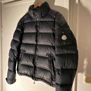 Moncler chavelier jacka  - Svart pufferjacka från Moncler i storlek 2 vilket motsvara storlek S, två dragkedjefickor och ikonisk logga på ärmen. Jackan är dunfodrad och har en snygg, quiltad design som ger en schysst siluett. Perfekt för kalla dagar och har en clean look som funkar till allt.