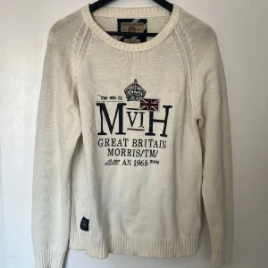 Vit stickad tröja Morris Gent's M - Snygg vit stickad tröja från Morris Gent's med tryck och broderad Union Jack-flagga framtill. Tröjan har rund halsringning, långa ärmar och ribbade muddar. Perfekt för dig som gillar klassisk brittisk stil och vill ha något som sticker ut.