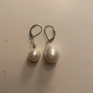 Silvriga örhängen med vita pärlor - Ett par unika örhängen med olika form på pärlorna, en rund och en droppformad. Örhängena är helt oanvända! Vet ej märket på dom dock. Köpte dom för 200kr❤️