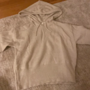 Beige hoodie med huva och snörning - Säljer en beige hoodie med huva och snörning. Tröjan har en avslappnad passform och är tillverkad i ett mjukt material som passar perfekt för chill dagar. Enkel och stilren design utan tryck eller mönster, med korta ärmar för en modern look.