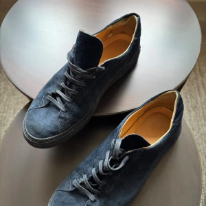 Mörkblå mocka sneakers från C.QP - Snygga mörkblå sneakers från C.QP, tillverkade i Portugal. Skorna har en rund tå, platt sula och är gjorda i mjuk mocka med skinnfoder i beige. Klassisk snörning framtill och stilren design som passar till jeans eller chinos.