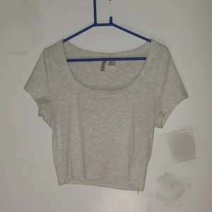 Ljusgrå croppad topp från H&M Divided - Säljer en ljusgrå croppad topp från H&M Divided. Toppen har rundad halsringning, korta ärmar och är tillverkad i mjuk ribbad bomull. Perfekt för dig som gillar enkel och clean stil. Passar dig som vill ha en basic topp med snygg passform.