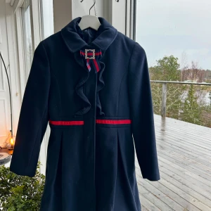 Mörkblå kappa med rosett och volang! ❤️❤️ - Snygg mörkblå kappa med röd detalj vid midjan och en dekorativ rosett med pärlor och volang framtill. Kappan har lång ärm och en klassisk krage som ger en elegant vibe. Perfekt för dig som gillar stilrena och unika plagg. ❤️❤️ skriv gärna vid funderingar och intresse! 🌟💫