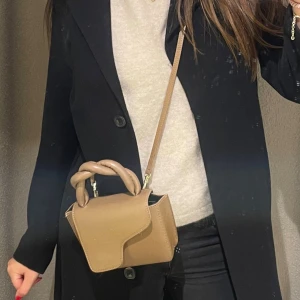 Brun handväska från ATP Atelier - Säljer en snygg brun handväska från ATP Atelier med flätat handtag och axelrem. Väskan är tillverkad i skinn och har en unik asymmetrisk lockdesign. Perfekt storlek för det viktigaste och en stilren look som lyfter din outfit.