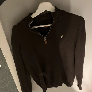 Stickad tröja Morris S - Mörkbrun stickad tröja från Morris med halv dragkedja och ribbad krage. Liten broderad logga på bröstet. Knappt använd och är därmed i ett bra skick. Bara att höra av sig vid minsta lilla fråga.