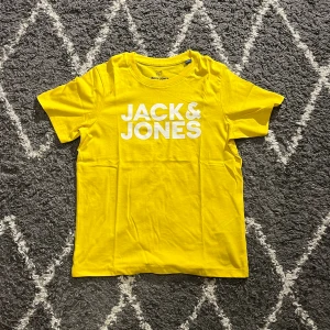 Gul t-shirt från Jack & Jones - Gul t-shirt från Jack & Jones med vit logotyptryck på bröstet. Klassisk rund halsringning och korta ärmar. Tillverkad i mjuk bomull som känns skön mot huden. Perfekt för dig som gillar färgstarka och stilrena plagg.
