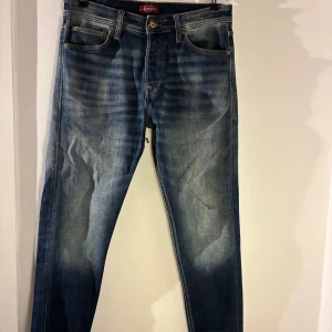 Jack & Jones – Tapered/Erik jeans (stl 32/32) - Säljer ett par blå jeans från Jack & Jones i modellen Tapered/Erik. Jeansen har en avsmalnande passform, klassisk femficksdesign och en snygg tvätt med naturliga slitningar. Storlek 32/32. De är använda men i bra skick utan hål eller skador. Nypris 699 kr.