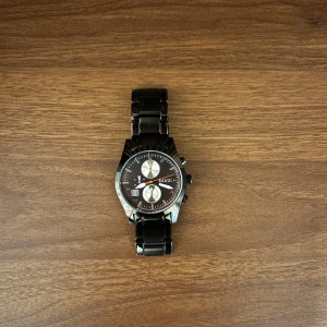 Svart klocka från Hugo Boss - Snygg svart kronografklocka från Hugo Boss med metallarmband och rund urtavla. Urtavlan har silverfärgade detaljer, datumvisning och tre mindre subdials. Klockan har en stilren och modern look som passar perfekt till dig som gillar accessoarer med edge. Kom dm för frågor🧐 pris kan diskuteras. 