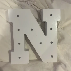 Bokstavslampa N LED - Dekorativ LED-lampa i form av bokstaven N, vit färg. Batteridriven med plats för AA-batterier på baksidan. Kan hängas på vägg eller ställas på hylla. Mindre repor och slitage syns, men i gott skick. Perfekt som nattlampa eller dekoration.