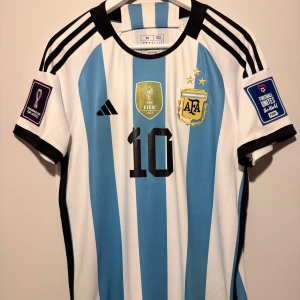 Argentina Messi VM 2022 fotbollströja - Jag har ej haft på mig denna tröja alls och endast hängt upp den i mitt rum för att det passar för grabbar att allmänt hänga upp dem någonstans i rummet, vem vill inte ha goat tröjan upphängd i sitt rum eller på sig  