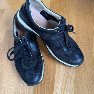 Svarta Gabor Rollingsoft sneakers med mesh - Svarta sneakers från Rollingsoft Sensitive med cool meshpanel och detaljer i skinn. Skorna har snörning, rund tå och en vit kontrasterande sula med grovt mönster undertill. Perfekt för dig som gillar sportig stil och vill ha bekväma skor med snygg design.