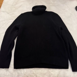 Svart polotröja från H&M, stickad - Svart stickad polotröja från H&M i regular fit. Tröjan har lång ärm och en hög, mjuk polokrage som ger en chill vibe. Perfekt för kalla dagar och enkel att matcha med jeans eller kjol. Materialet är skönt och håller värmen bra.