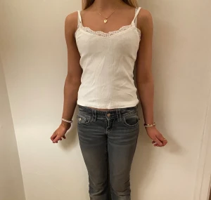 Vit ribbad linnetopp med spets H&M - Säljer en vit ribbad linnetopp från H&M i storlek 146/152. Toppen har smala axelband och v-ringning med söt spetskant upptill. Perfekt att styla med jeans eller kjol för en fräsch look.