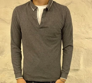 Grå pikétröja från Massimo dutti - Snygg grå långärmad pikétröja med klassisk krage och knappslå. Tröjan har vita detaljer vid kragen och ärmsluten som ger en fräsch kontrast. Perfekt för dig som gillar stilrena och enkla plagg med lite edge.