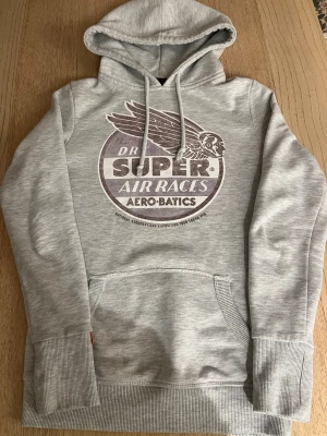 Grå Superdry hoodie - Grå Superdry hoodie med snyggt och unikt tryck, storlek XS, nypris ca 699 kr. Priset är inte hugget i sten. Tveka inte att höra av dig vid minsta fundering!