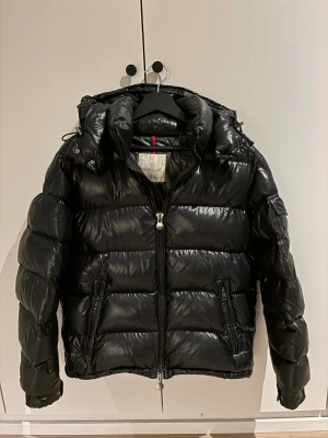 Svart pufferjacka från Moncler - Säljer en svart pufferjacka från Moncler med glansig finish och huva. Jackan har dragkedja framtill, två sidofickor med dragkedja och en klassisk Moncler-logga på ärmen. Perfekt för kalla dagar och riktigt snygg streetstil. den är helt äkta kvitto finns och pris kan diskuteras.