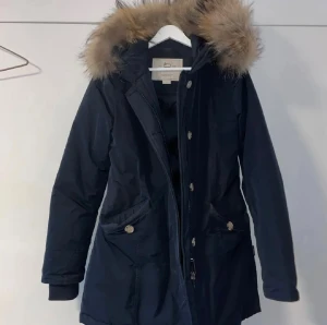 Woolrich - Vinterjacka - Säljer en mörkblå parkas från Woolrich i storlek S. Jackan har en stor huva med äkta päls. Perfekt för kalla dagar och riktigt snygg till vintern. Pris kan diskuteras.