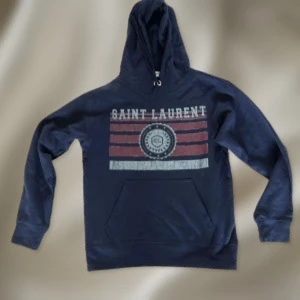 Mörkblå Saint Laurent hoodie - Snygg mörkblå hoodie från Saint Laurent med tryck framtill i vitt och rött. Tröjan har huva med snörning och en stor magficka. Perfekt för dig som gillar streetwear och vill ha en cool look. Passar dig som vill sticka ut med ett klassiskt märke. PRISET KAN DISKUTERAS 