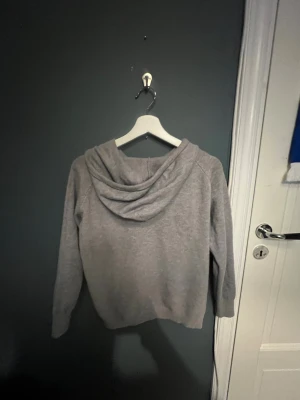 Grå hoodie med snörning - En enkel och stilren grå hoodie med huva och snörning framtill. Tröjan har långärmade ärmar och en klassisk passform som funkar till de flesta outfits. Mjuk och skön marinoull, perfekt för chill dagar eller när du vill ha något bekvämt.