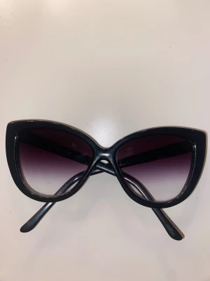 Svarta cat eye solglasögon Cheap Monday - Snygga svarta solglasögon från Cheap Monday med klassisk cat eye-form. Bågarna är i plast och har mörka, tonade linser som går från svart till lila. Perfekt accessoar för att lyfta din look och ge lite edge.