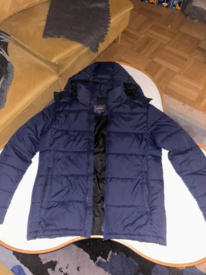 Mörkblå pufferjacka från Dressmann - Nypris 2000 mitt pris 700. Säljer en mörkblå pufferjacka från Dressmann i storlek M. Jackan har huva, dragkedja och två sidofickor. Materialet är syntet och jackan är quiltad för extra värme. Perfekt för kalla dagar och har en clean, modern look.