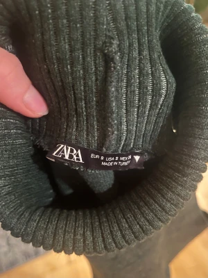 Mörkgrön stickad väst från Zara - Snygg mörkgrön stickad väst från Zara med hög polokrage och ribbade detaljer. Västen är ärmlös och har en loose fit, perfekt att slänga över en skjorta eller t-shirt. Bra skick, säljs för den kom i fel storlek. Jag har aldrig använt men jag köpte det begagnad.