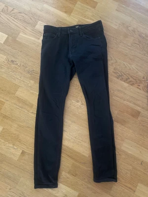 Svarta Lee Malone jeans W31 L32 - Svarta jeans från Lee, modell Malone, med smal passform. Jeansen har normal midja och raka ben, tillverkade i mjukt och stretchigt bomullsmaterial. Perfekta för dig som gillar stilrena och enkla svarta jeans. Jeansen har inga defekter och är i bra skick.
