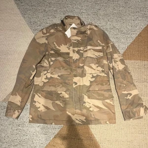 Jacka från Zadig & Voltaire - Snygg camouflagejacka från Zadig & Voltaire i beige och bruna toner. Jackan har flera stora fickor framtill, klassisk krage och raka ärmar. Den har en loose passform och är helt ny, tags sitter fortfarande på. Skick:10/10. Nypris: 4000kr, Mitt pris:1499kr