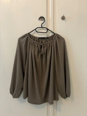 Beige blus med knytning - Beige blus i storlek S. Blusen har en luftig och flowy passform. Rundad halsringning med snygg knytning framtill. Materialet är lätt och har en diskret struktur som ger extra känsla. Sitter snyggare på än vad det ser ut hängandes på galge. Bara använd en gång. Nyskick.