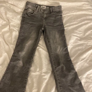 Grå bootcut jeans från 157, stl 150 - Snygga grå jeans från 157 i bootcut-modell med markerade sömmar och coola fickdetaljer bak. Klassisk femficksdesign, dubbla knappar i midjan och slitningseffekt som ger en avslappnad vibe. Perfekt för dig som gillar retrostil och vill sticka ut.