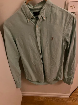 Ljusgrön skjorta från Polo Ralph Lauren - Fräsch ljusgrön skjorta från Polo Ralph Lauren i slim fit-modell. Klassisk button-down krage, långärmad och med broderad logga på bröstet. Skjortan är tillverkad i mjuk bomull och har knappar framtill och vid ärmslut. Perfekt för dig som gillar stilrena plagg med snygg passform.