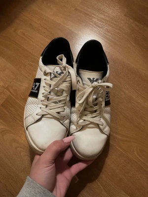 Emporio Armani EA7 vita sneakers - Säljer mina snygga vita sneakers från Emporio Armani EA7 med svarta detaljer och perforerat mönster på sidorna. 