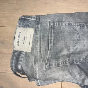 Grå skinny jeans från Jack & Jones - Snygga grå jeans från Jack & Jones med klassisk femficksdesign och diskret tvättad look. Modellen är skinny med smal passform hela vägen ner och tillverkad i mjukt jeanstyg. Perfekt för dig som gillar en modern och stilren vibe. Det är bra skick på jeansen och passar bra en som är 170-180