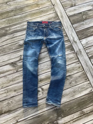 Replay Jondrill jeans blå 34/32 - Säljer ett par Replay Jondrill jeans i klassisk blå tvätt med snygga slitningar och lätt ruffad look. Modellen har raka ben, fem fickor och kontrastsömmar. Materialet är slitstarkt jeans och passformen är normal. Perfekt för dig som gillar en cool och avslappnad stil.