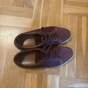 Vinröda mockasneakers från Loro Piana - Snygga vinröda sneakers från Loro Piana, modellen Freetime Walk. Skorna har en låg profil, rund tå och platt sula. Tillverkade i mjuk mocka med skinnfoder och snörning framtill. Perfekt för dig som gillar stilrena och lyxiga sneakers med italiensk känsla.