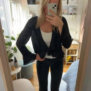 Svart omlottblus med knyt från Gina Tricot - Svart omlottblus från Gina Tricot i storlek 40. Blusen har långa, lite utsvängda ärmar och en  knytning framtill. Materialet lite transparent. Fint skick!!!