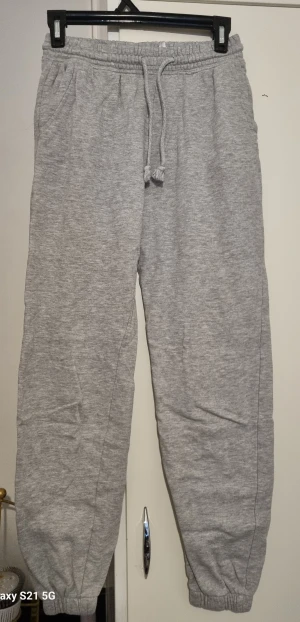 Grå mjukisbyxor med snörning - Säljer ett par grå mjukisbyxor med elastisk midja och snörning. Byxorna har ribbade muddar vid bensluten och sidofickor. Perfekta för chill dagar eller när du vill vara extra bekväm. Materialet är mjukt och känns skönt mot huden.