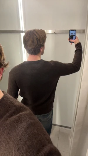 Brun stickad tröja med rund hals - Mysig brun stickad tröja med rund halsringning och lång ärm. Tröjan har en enkel och stilren design utan synliga detaljer eller mönster, perfekt för lager-på-lager under kyliga dagar. Storlek M