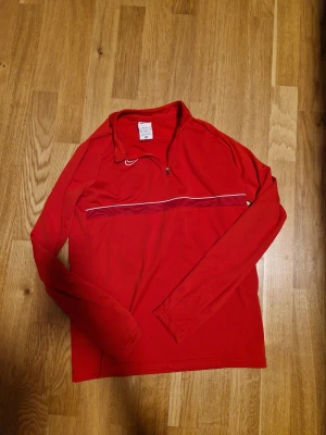 Röd Nike Dri-Fit half zip tröja - Snygg röd långärmad tröja från Nike i Dri-Fit material, perfekt för träning. Skön passform och sportig look.