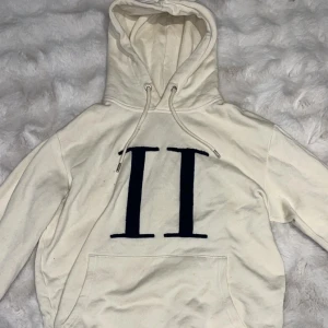 Les Deux hoodie  - Säljer en snygg vit hoodie från Les Deux med stort svart 'II'-tryck på bröstet. Tröjan har huva med snörning, känguruficka och är tillverkad i mjuk bomull. Perfekt för dig som gillar clean och stilren streetwear.